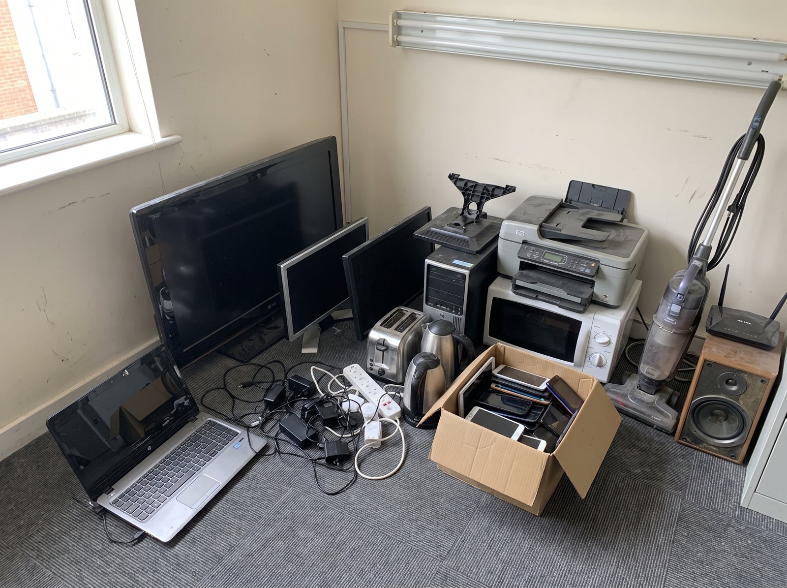 Storeroom corner piled with old monitors and printers, before
